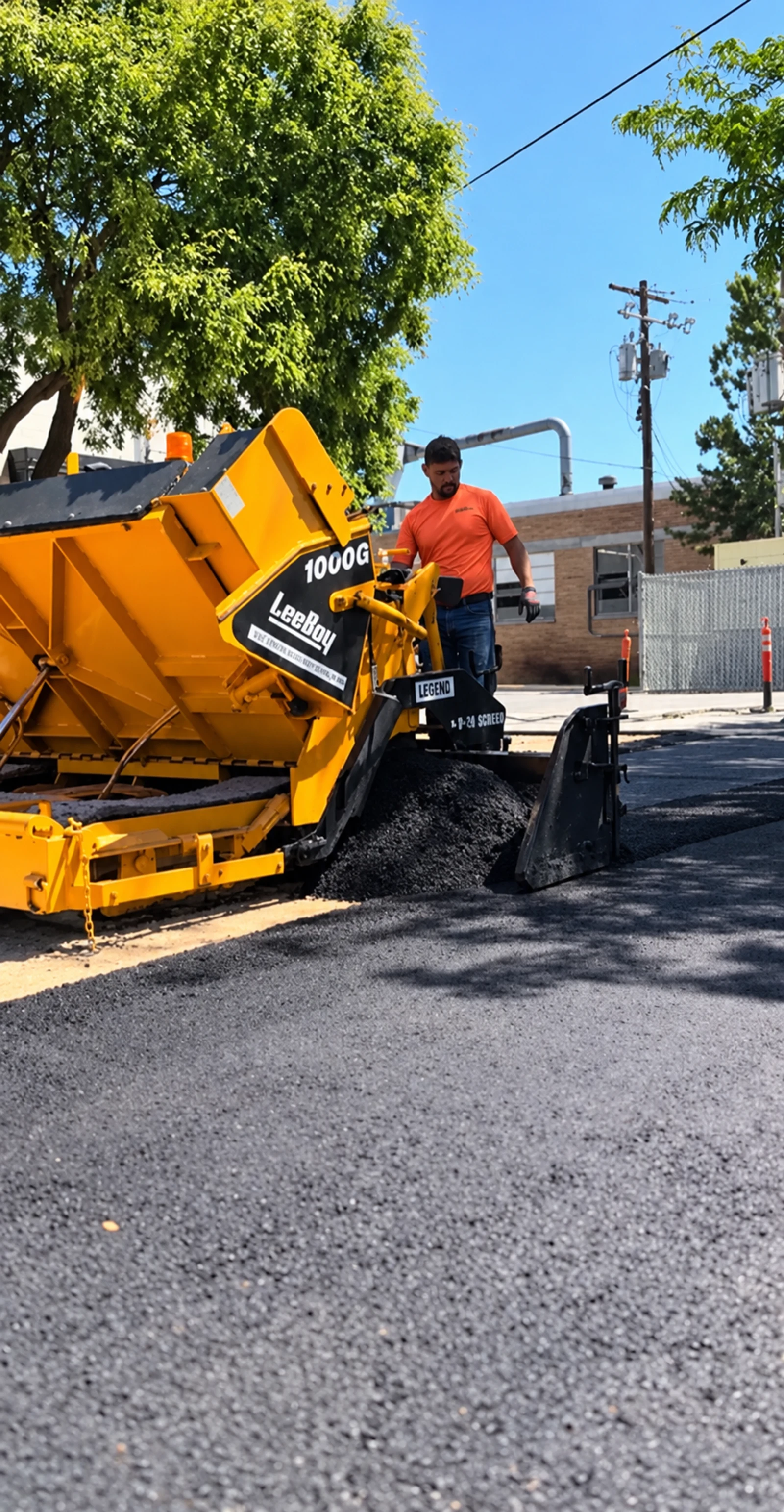 Crew members beside a yellow paving machine and a dark paved surface.